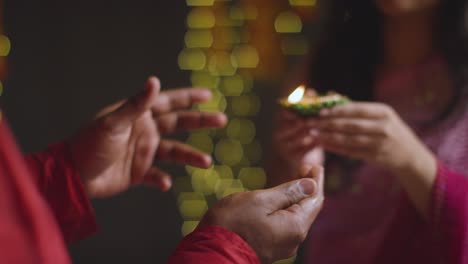 Close-Up-Of-Woman-Handing-Lit-Diya-Oil-Lamp-To-Man-Celebrating-Festival-Of-Diwali